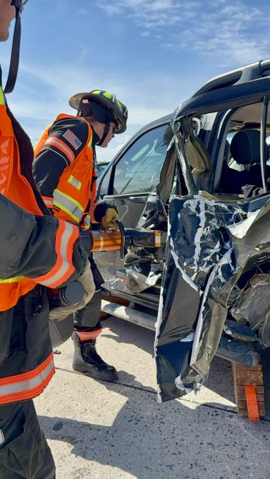 Daytime image of firefighter using large power tools to get a person out of a damaged vehicle