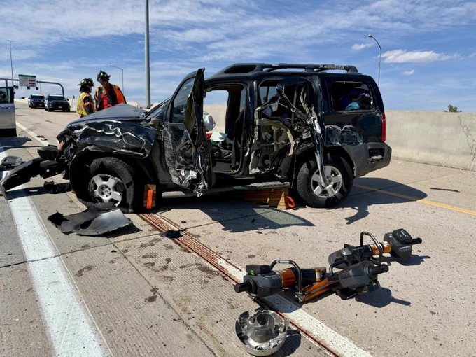 Daytime image of a damaged vehicle on a highway with firefighters nearby