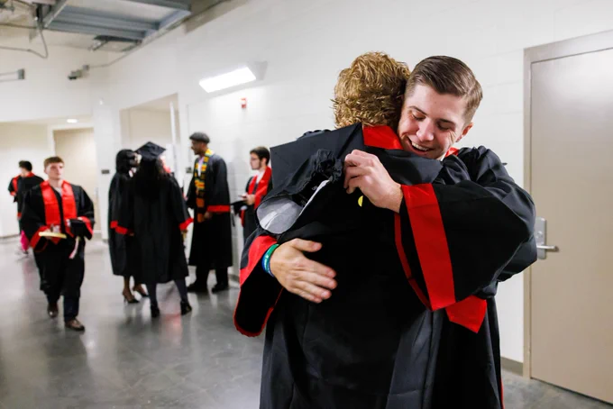 Two male graduates embrace in a hallway of Pinnacle Bank Arena. Other graduates can be seen in the background. (Jordan Opp/University Communication and Marketing)