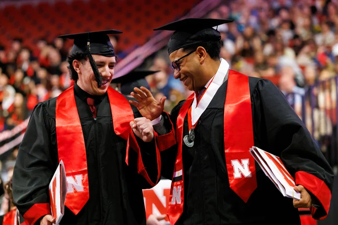 Two students congratulate each other with a high-five fist bump after receiving their diplomas