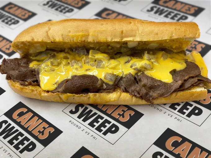 Photo of a cheesesteak on paper that has a restaurant sign that says Canes Sweep