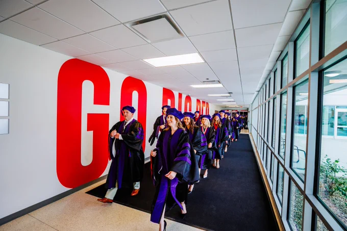 Law graduates walk down a hallway in the Devaney Center with large "Go Big Red" letters on the wall behind them