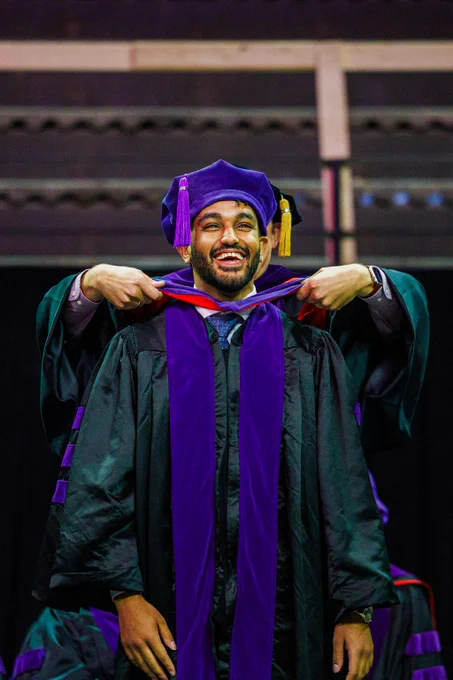 A purple and red hood is placed over the head of a smiling College of Law graduate