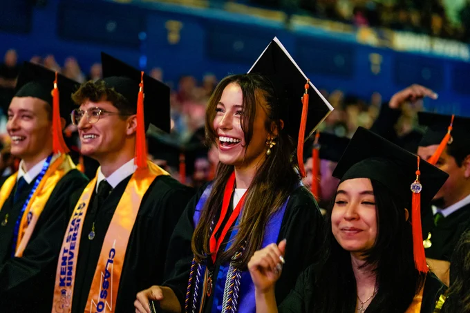 Joy fills the arena as Kent State University graduates laugh and cheer together during commencement, their orange tassels swaying with excitement.