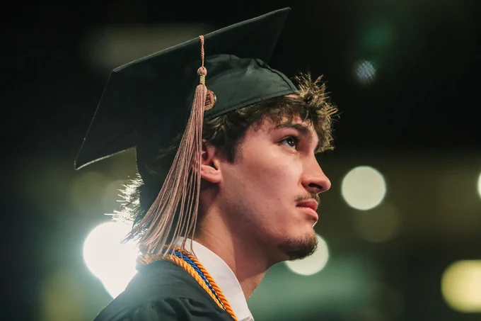 A graduate gazes forward with quiet determination during the Kent State University commencement ceremony, his honor cords catching the light.