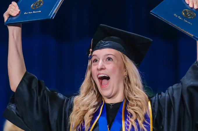 Pure elation — a graduate thrusts her Kent State diplomas high in the air, her wide-open smile saying everything words cannot.