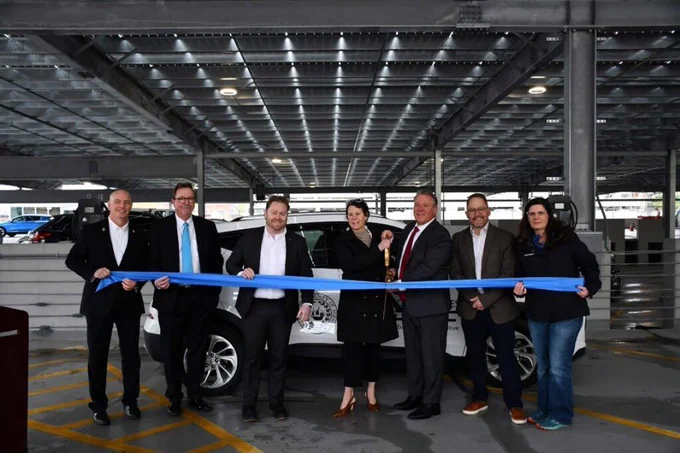 Seven people posing for a ribbon-cutting ceremony in a parking garage.