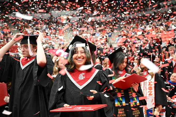 Color indoor photo of grads having crimson and gray confetti raining down on them. 