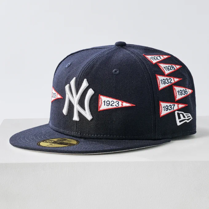 Dark blue Yankees hat featuring pennant patches of years the team has won the World Series. The New Era logo is on the lower portion of the left-side panel. A gold and black New Era sticker is on the top of the bill.