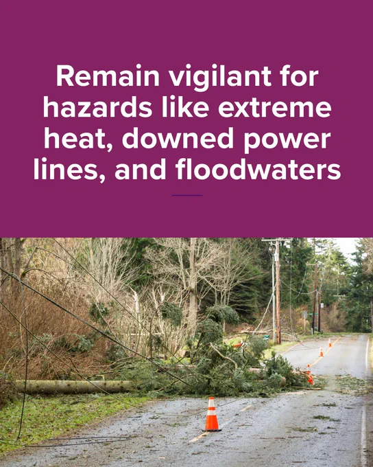 A rural road is blocked by a fallen tree and power lines, with orange cones indicating the hazard. Text above the image warns to remain vigilant for hazards like extreme heat, downed power lines, and floodwaters.