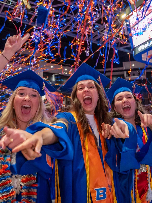 Boise State graduates cheering at the Spring 2026 
Commencement with orange and blue streamers behind them.

