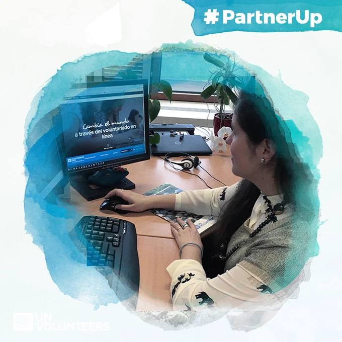 Person using a computer to access an online volunteering platform with Spanish text encouraging global change through volunteering.