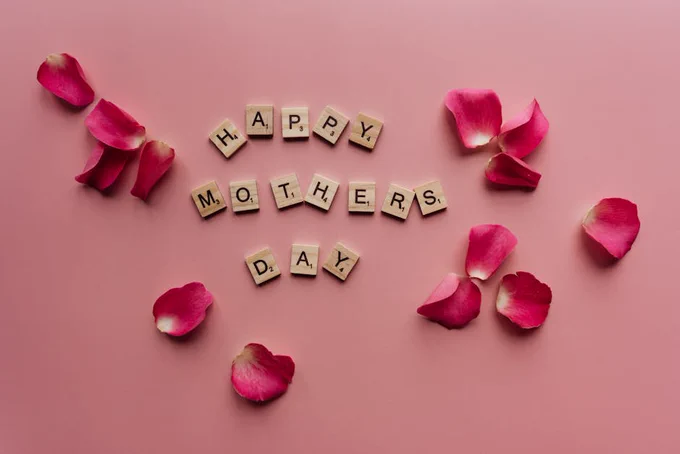 Scrabble tiles spelling 'Happy Mother's Day' surrounded by pink petals.
