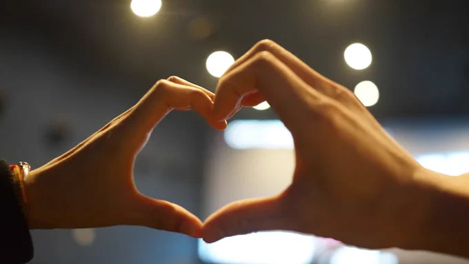 Close-up of hands forming a heart shape in ambient light, symbolizing love and connection.