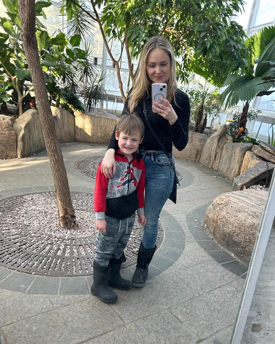 A mother and her son posing for a mirror selfie surrounded by lush tropical plants and trees inside the Butterfly Gallery