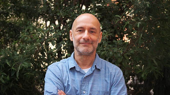 Jose Alonso, William Neal Reynolds Distinguished Professor in the NC State Department of Plant and Microbial Biology, standing outdoors with arms crossed in front of leafy green bushes. 
