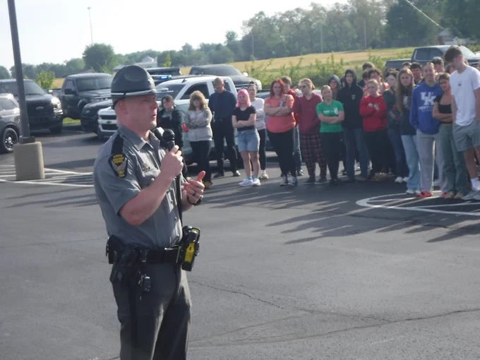 A trooper is standing in front of students outside at Eastern Brown High School. The trooper is giving a Drive to Live presentation. 