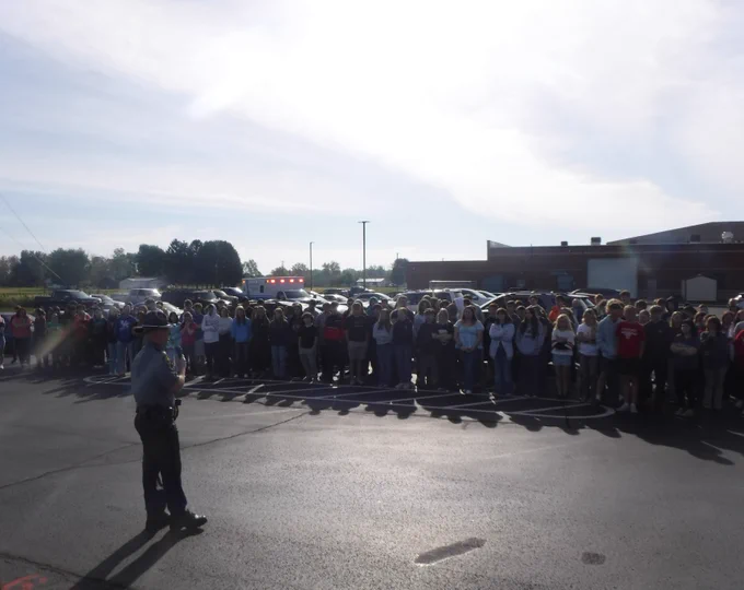 A trooper is standing in front of students outside at Eastern Brown High School. The trooper is giving a Drive to Live presentation. 