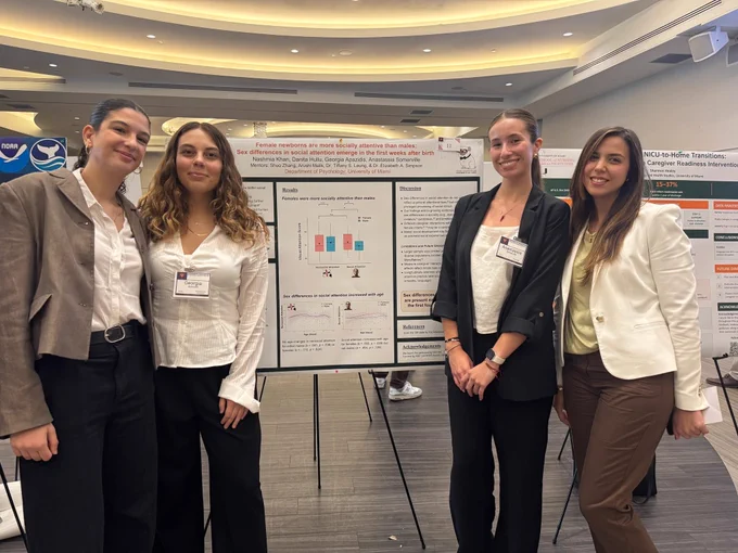 Four women standing front of a research poster smiling. The title of the poster says: female newborns are more socially attentive than males.