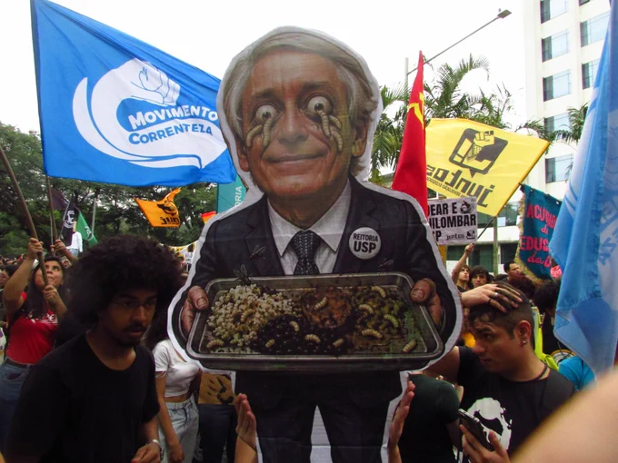 Um cartaz com o rosto de Aluísio Segurado, reitor da Universidade de São Paulo (USP), servindo uma bandeja com larvas e comida estragada. Créditos: Gabriel Albuquerque