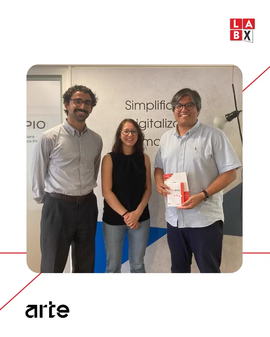 Três pessoas em pé, sorrindo, na sede da ARTE. À esquerda e ao centro estão dois colaboradores do LabX; à direita, um representante do Governo de Goiás. No canto superior direito, aparece o logótipo do LabX e, na parte inferior, o logótipo da ARTE.