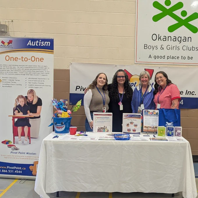 Four Pivot Point team members smiling behind their event table at Vernon's Neurodiverse Family Fun Day: Paige Morrison BCBA, Shannon Moorhead (Okanagan Regional Manager), Heather McIntosh (L.I.F.E. Services Coach), and Avery Kugler BC-p.