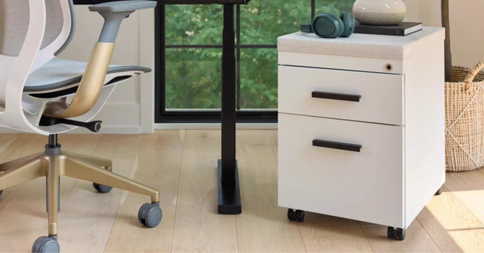 Modern white office chair with gold base next to a white rolling drawer unit under a desk by a window.
