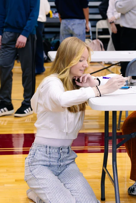 A CHS student kneels at a folding table to fill out a questionnaire. 
