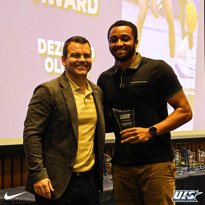 Dezmond Olivier stands with a coach at the Night of the Stars banquet, holding his Star Spirit Award trophy in front of a presentation screen displaying his name.