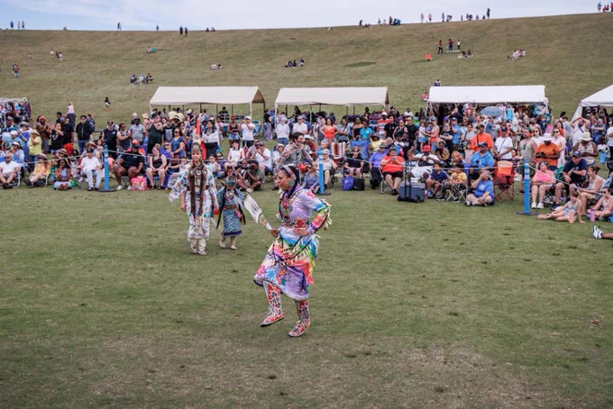 A group of people is watching a Native American performance at Mount Trashmore