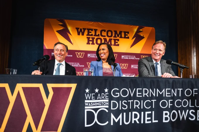 Photo of Josh Harris, Muriel Bowser and Roger Goodell sitting together. Behind them is a press backdrop that reads Welcome Home. 