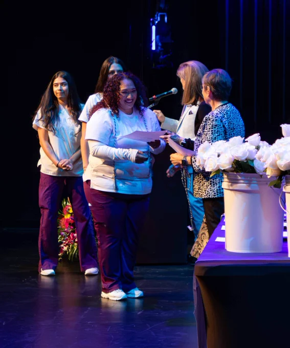 An FSW nursing student smiles as she receives a graduation cord and certificate at the nurse pinning ceremony.