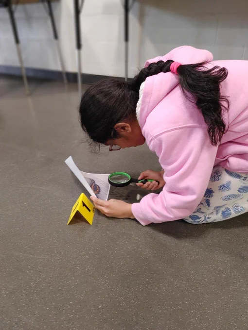 Person wearing a pink hoodie sitting on the floor and examining something intently with a magnifying glass.