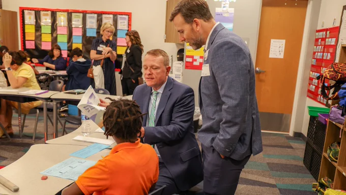 Two adults helping a child with an activity.
