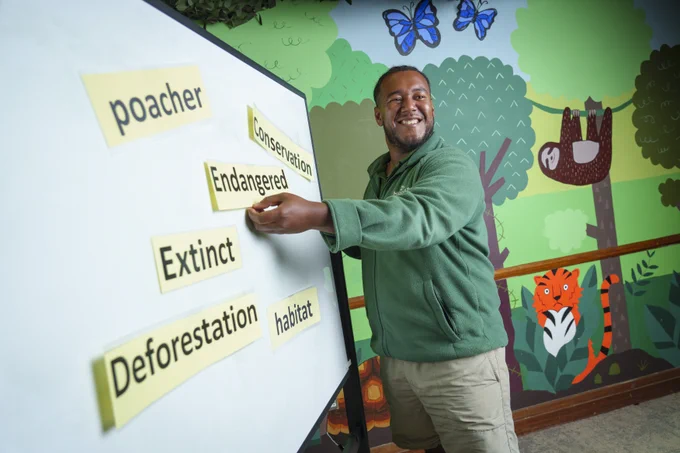 Person arranging words like poacher, conservation, and deforestation on a whiteboard in a colorful wildlife-themed room.