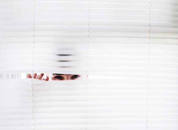 A person peeks through white blinds, creating an intriguing sense of curiosity.
