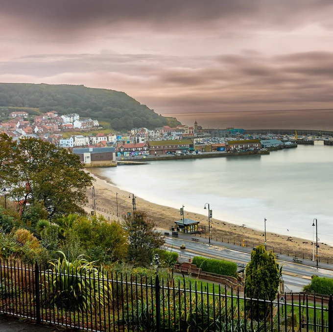 Scarborough with the harbour, beach, and hill under a cloudy sky.