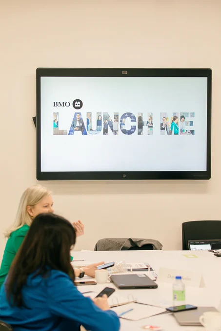 People sit at a desk beneath a screen that reads BMO Launch Me.
