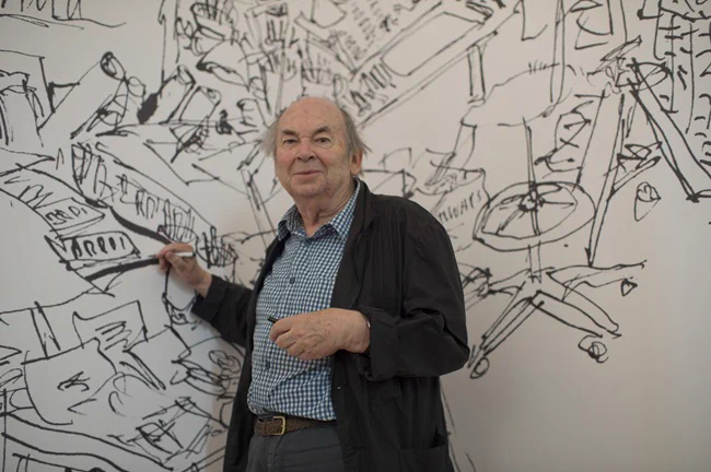 A photograph of illustrator Quentin Blake in front of sketches on a wall at the new Quentin Blake Centre for Illustration. 