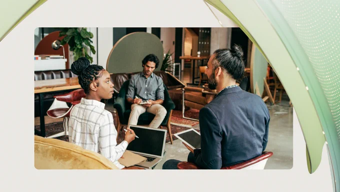 Two men and a woman sitting in an office space with computers on their laps talking