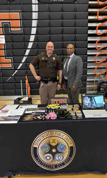Iowa Department of Public Safety officers standing behind a table with safety materials and informational brochures in a gymnasium.