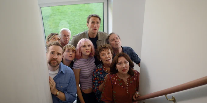 From Trying. The ensemble cast of Trying including Rafe Spall as Jason stand huddled together at the bottom of a staircase, looking upward with quizzical expressions on their faces.
