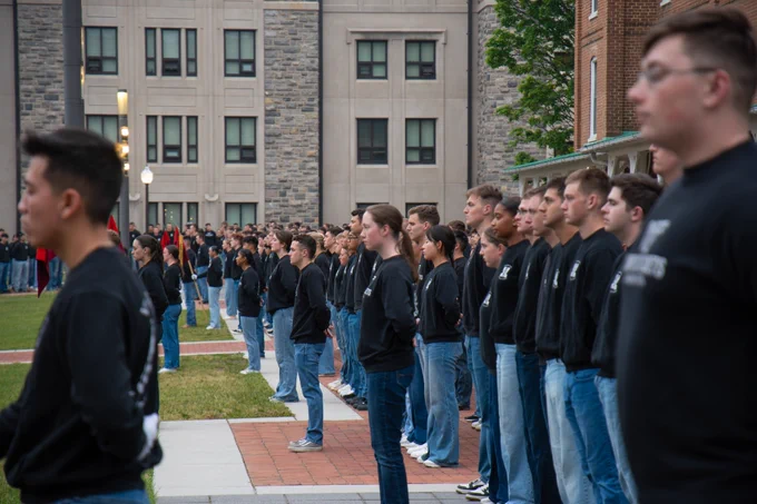 A close view of cadets wearing black shirts and blue jeans standing shoulder to shoulder along a brick walkway, facing forward during a formation.