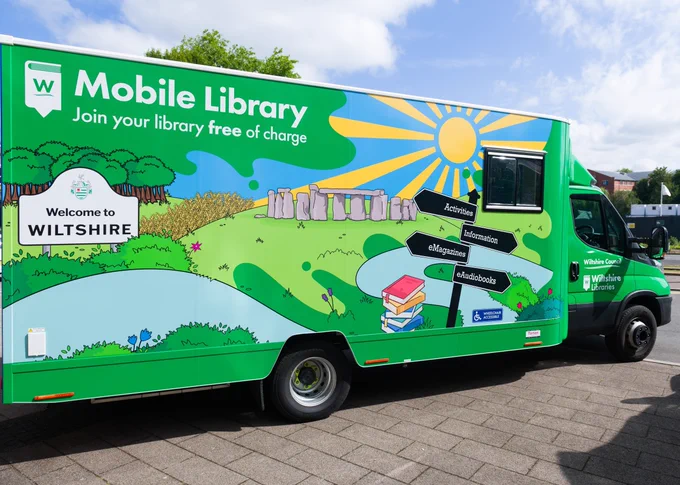 A Wiltshire Libraries green mobile library van with countryside and Stonehenge mural.