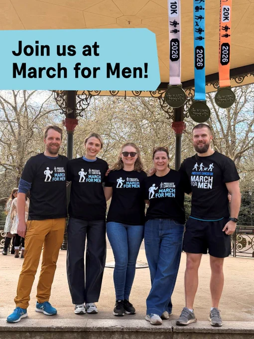 A group of people standing together in a park, wearing matching 'March for Men' shirts. They are smiling at the camera with medals hanging above. Overlay text reads 'Join us at March for Men!' Trees and a clear sky are in the background.