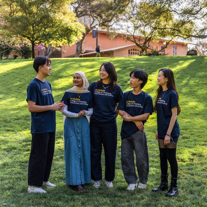A group of students wearing UC Berkeley College of Computing, Data Science, and Society t-shirts, smiling and talking outside.