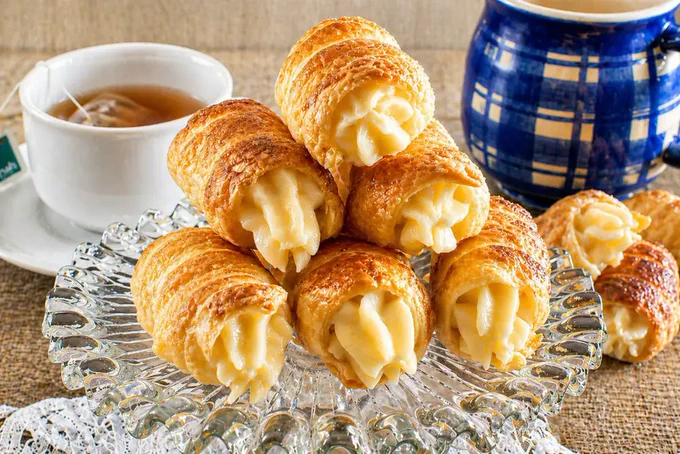 Golden puff pastry cannoncini served with hot tea and a blue ceramic coffee pot.