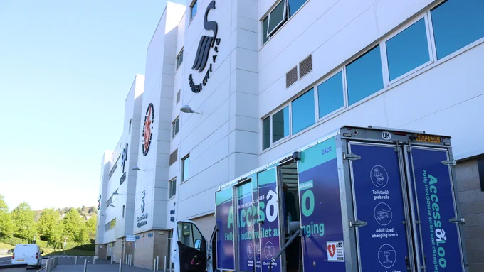 The front of the Swansea.com Stadium, with a large Swansea City logo on the wall and an Accessoloo van in front.