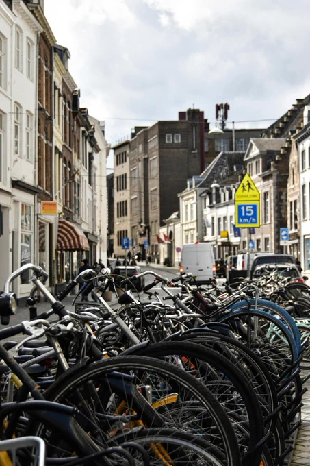 Bicycles parked along a busy urban street under a cloudy sky in a bustling city center.