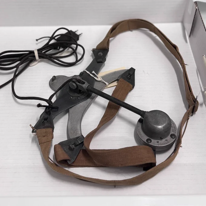 Casque vintage avec un microphone en métal et des sangles réglables marron, présenté dans une boîte blanche sous un tiroir.